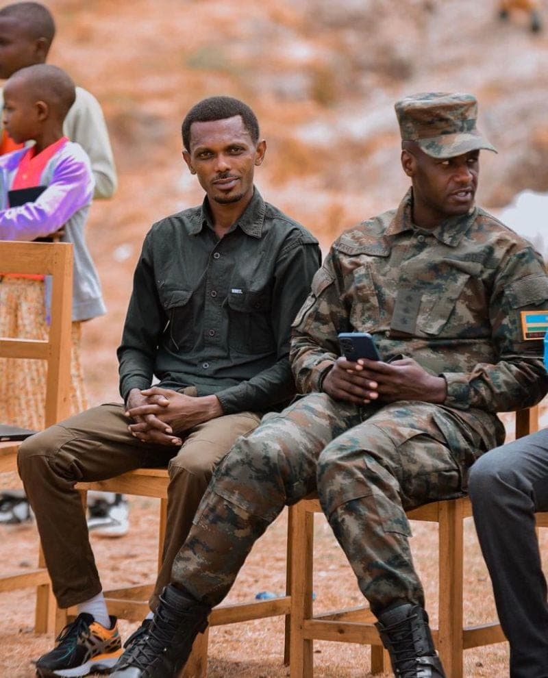 Cyusa Ian Berulo seated with a Rwandan officer and children at a Murengere Atararenga event